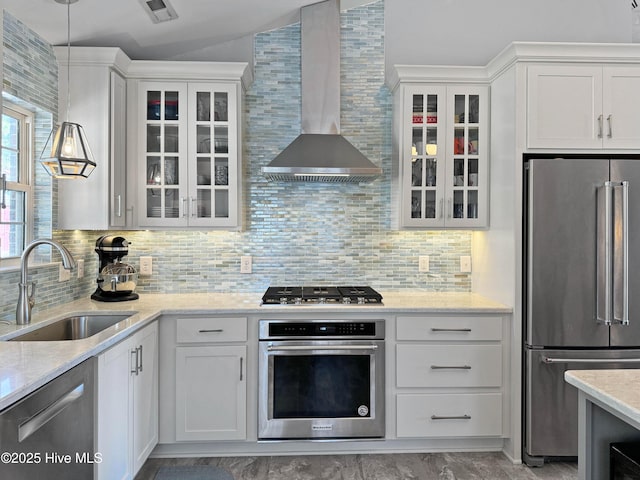 kitchen featuring wall chimney range hood, sink, appliances with stainless steel finishes, light stone countertops, and white cabinets