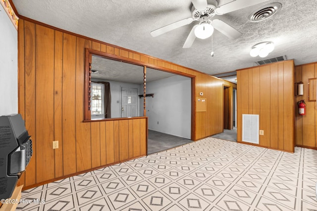 interior space with heating unit, wooden walls, light colored carpet, ceiling fan, and a textured ceiling