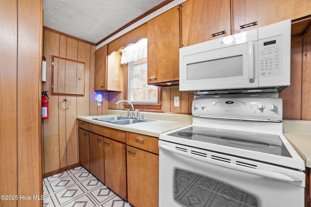 kitchen featuring white appliances, wooden walls, sink, and a textured ceiling