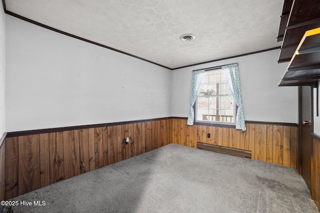 carpeted spare room featuring a baseboard radiator, ornamental molding, a textured ceiling, and wood walls