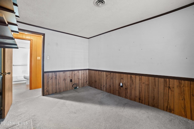 carpeted spare room featuring ornamental molding, a textured ceiling, and wooden walls