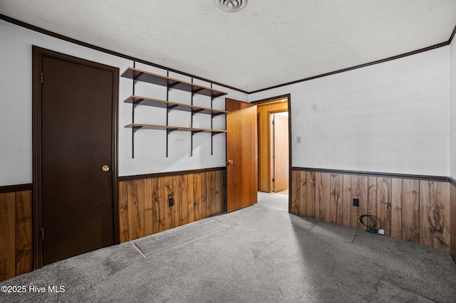 unfurnished room featuring crown molding, light carpet, a textured ceiling, and wooden walls