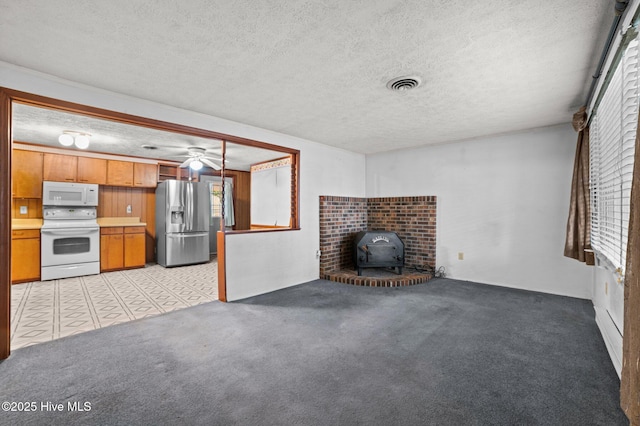 unfurnished living room featuring a wood stove, light colored carpet, and a textured ceiling