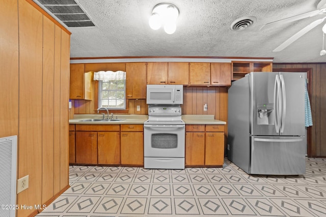 kitchen with sink, wood walls, white appliances, a textured ceiling, and ceiling fan