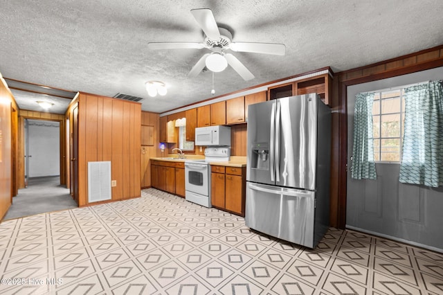 kitchen with ceiling fan, white appliances, sink, and wood walls