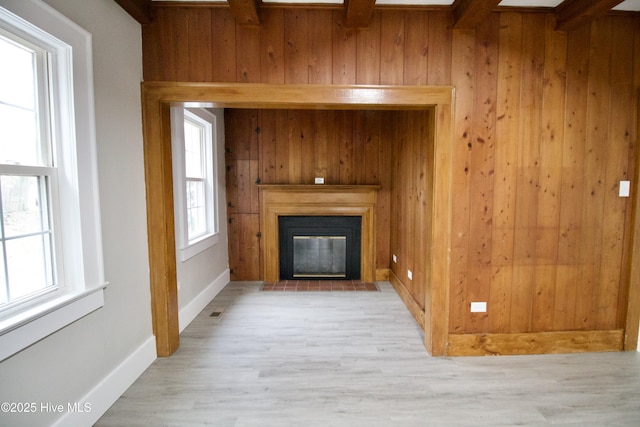 unfurnished living room featuring beamed ceiling, wooden walls, and light hardwood / wood-style flooring