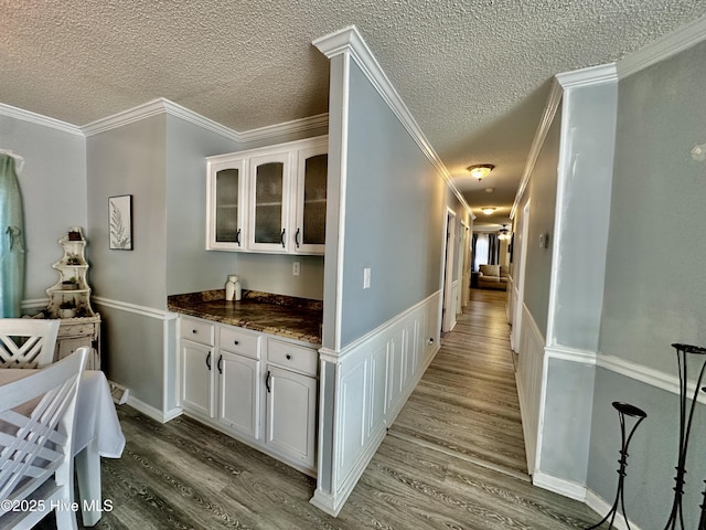 bar featuring crown molding, a textured ceiling, light hardwood / wood-style flooring, and white cabinets