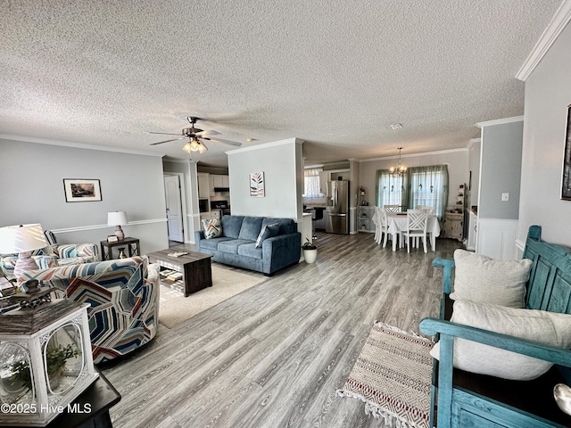 living room with crown molding, ceiling fan with notable chandelier, a textured ceiling, and light wood-type flooring