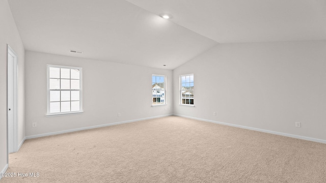 empty room featuring a healthy amount of sunlight, vaulted ceiling, and light carpet