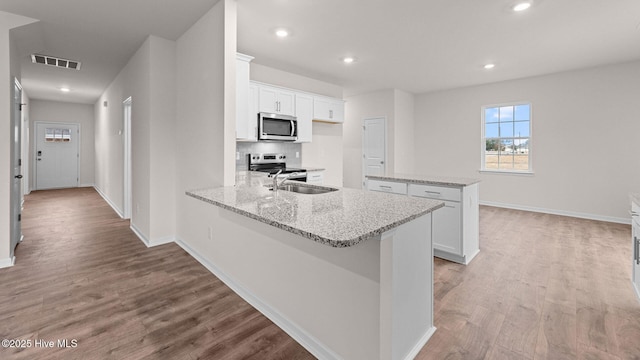 kitchen featuring a kitchen island, sink, white cabinets, light stone counters, and stainless steel appliances