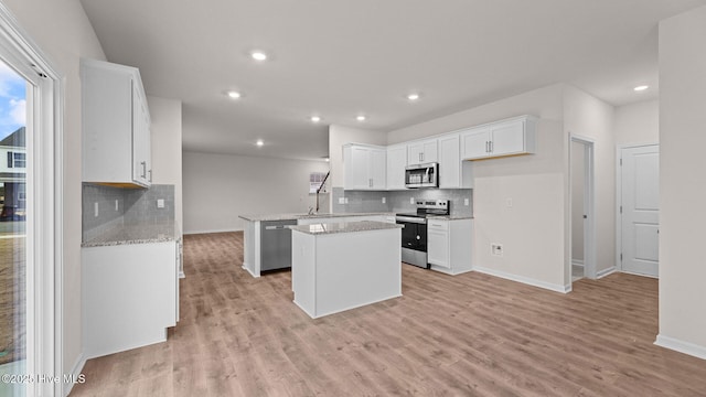 kitchen featuring a kitchen island, appliances with stainless steel finishes, white cabinets, kitchen peninsula, and light stone countertops