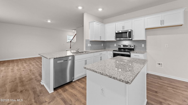 kitchen featuring sink, white cabinetry, stainless steel appliances, light stone countertops, and a kitchen island