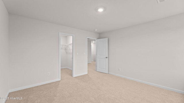 unfurnished bedroom with a walk in closet, light colored carpet, and a closet