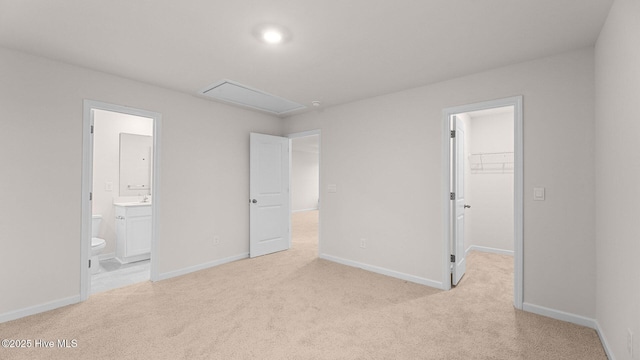 unfurnished bedroom with a spacious closet, light colored carpet, a closet, and ensuite bathroom