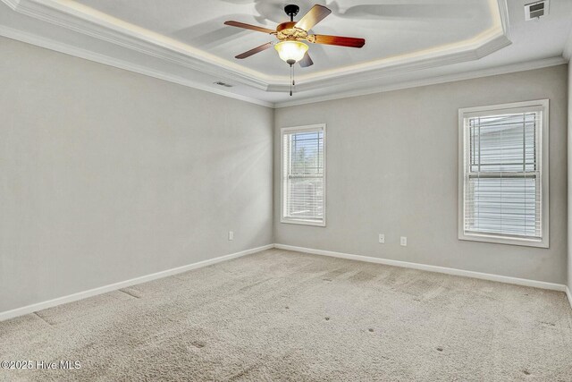 empty room with a tray ceiling, ornamental molding, and carpet flooring