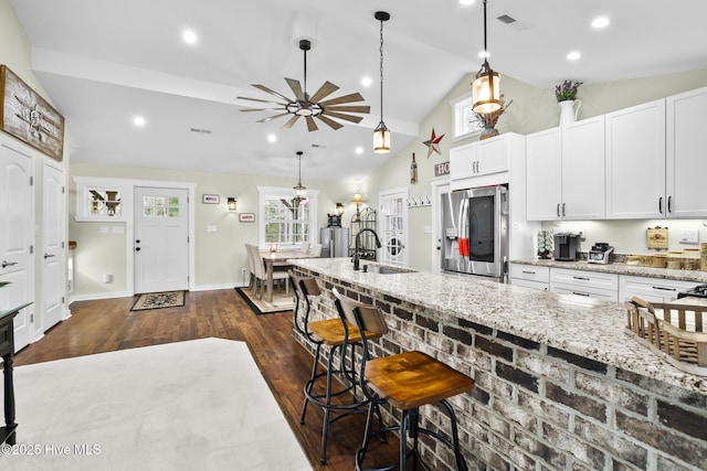 kitchen with white cabinetry, sink, stainless steel fridge, a kitchen bar, and light stone countertops