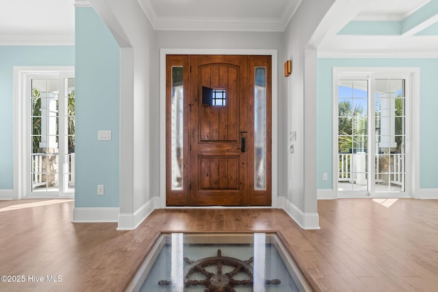 entryway featuring wood finished floors, crown molding, a healthy amount of sunlight, and arched walkways