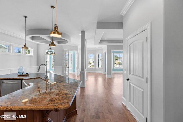 kitchen featuring wood finished floors, dark stone counters, an island with sink, ornamental molding, and a sink