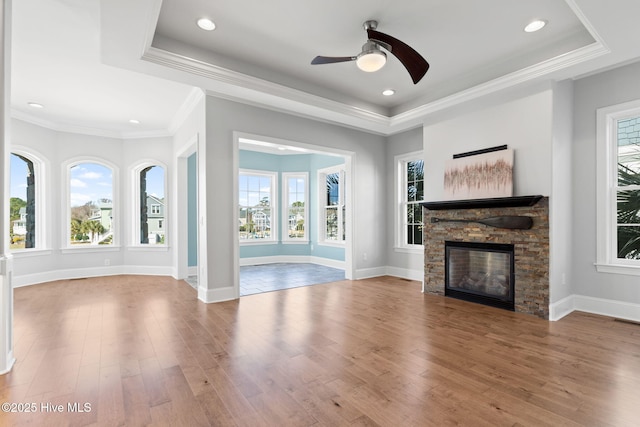 unfurnished living room with a stone fireplace, a tray ceiling, and a healthy amount of sunlight