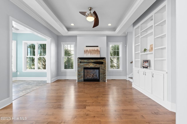 unfurnished living room with a tray ceiling, plenty of natural light, a fireplace, and wood-type flooring