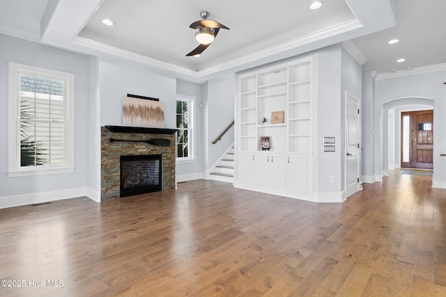 unfurnished living room featuring arched walkways, a fireplace, baseboards, and hardwood / wood-style flooring