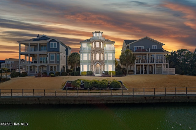 back of property featuring a balcony, fence private yard, a water view, and a lawn