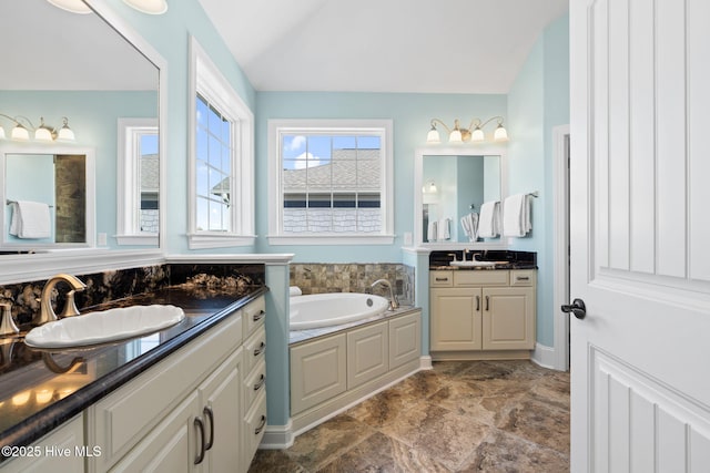 bathroom featuring a bath, vaulted ceiling, two vanities, and a sink