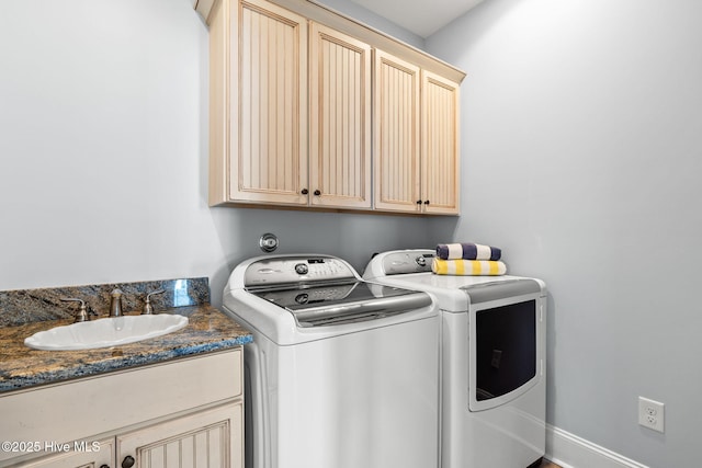 clothes washing area featuring a sink, cabinet space, baseboards, and washing machine and clothes dryer