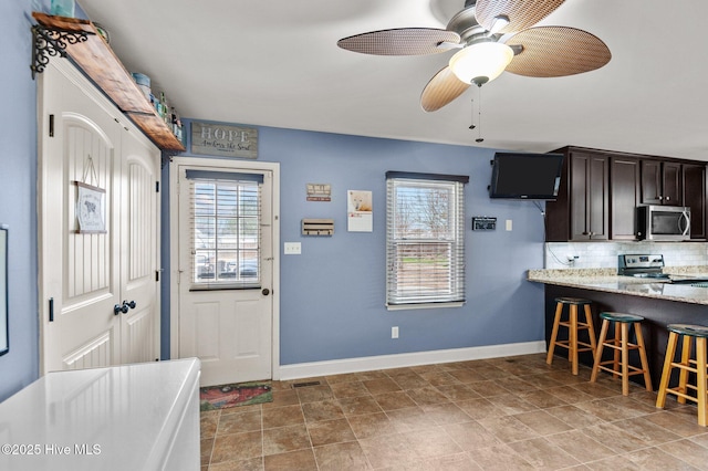 kitchen featuring ceiling fan, appliances with stainless steel finishes, backsplash, dark brown cabinets, and light stone countertops