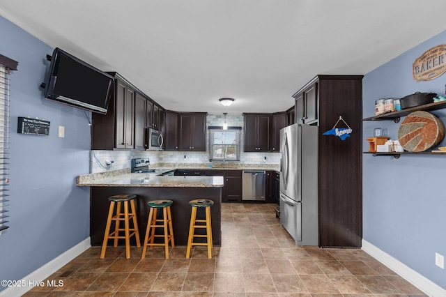 kitchen featuring tasteful backsplash, appliances with stainless steel finishes, a kitchen bar, and kitchen peninsula