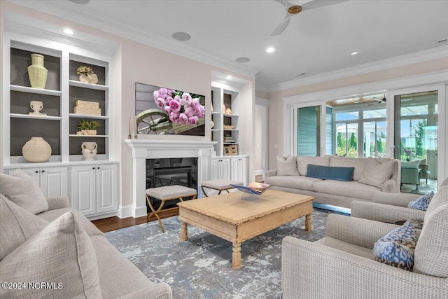 living area with a ceiling fan, a glass covered fireplace, ornamental molding, wood finished floors, and built in shelves