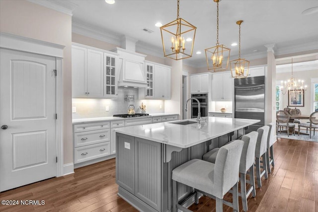 kitchen featuring white cabinets, light countertops, appliances with stainless steel finishes, an island with sink, and glass insert cabinets