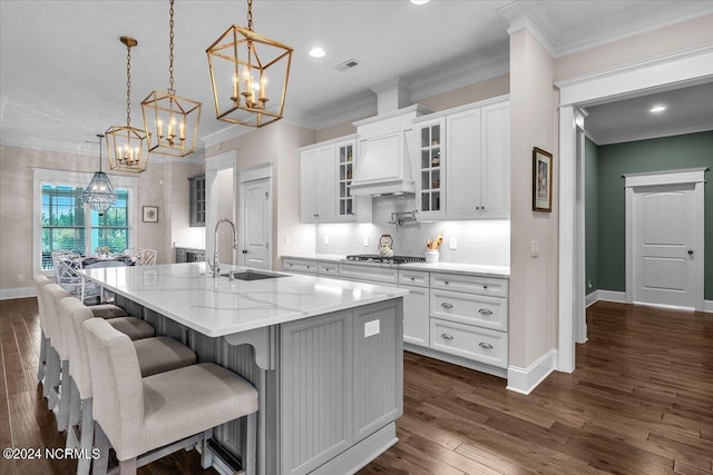 kitchen with a center island with sink, glass insert cabinets, hanging light fixtures, premium range hood, and white cabinetry