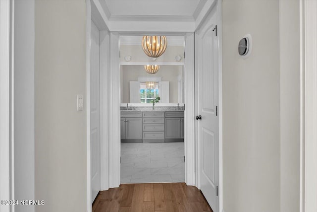 corridor with marble finish floor, crown molding, a sink, and an inviting chandelier