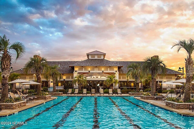 pool at dusk with a community pool and a patio