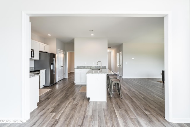 kitchen with a kitchen bar, sink, a center island with sink, light stone countertops, and white cabinets