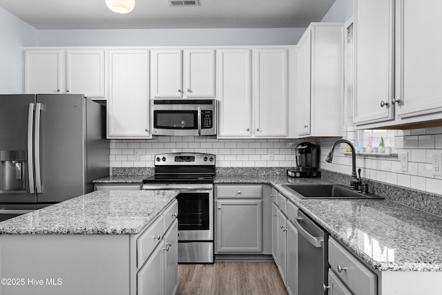 kitchen with light stone counters, appliances with stainless steel finishes, sink, and white cabinets