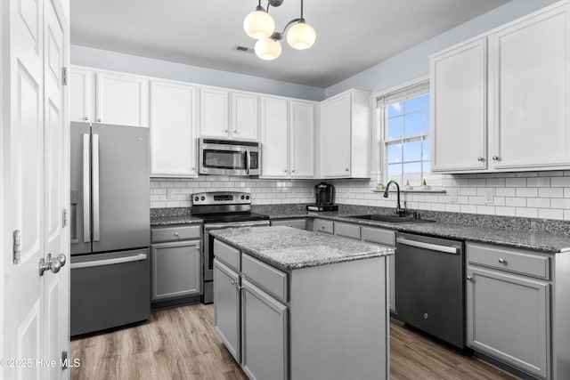 kitchen featuring appliances with stainless steel finishes, sink, gray cabinetry, hanging light fixtures, and a center island