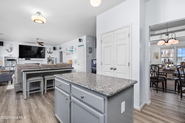 kitchen featuring ceiling fan with notable chandelier, hardwood / wood-style floors, a center island, light stone countertops, and decorative light fixtures