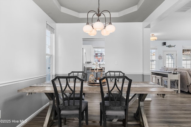 dining space featuring a raised ceiling, an inviting chandelier, and dark hardwood / wood-style flooring