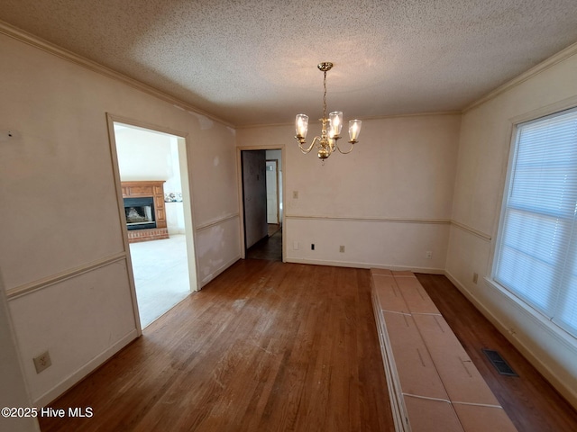 unfurnished dining area with hardwood / wood-style flooring, ornamental molding, a chandelier, and a textured ceiling