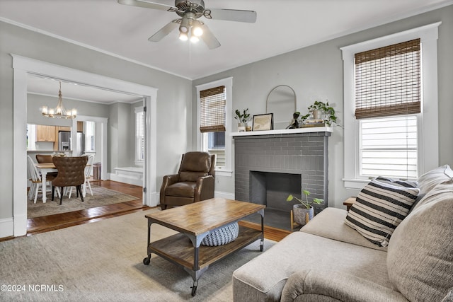 living room with a brick fireplace, hardwood / wood-style flooring, ceiling fan with notable chandelier, and ornamental molding