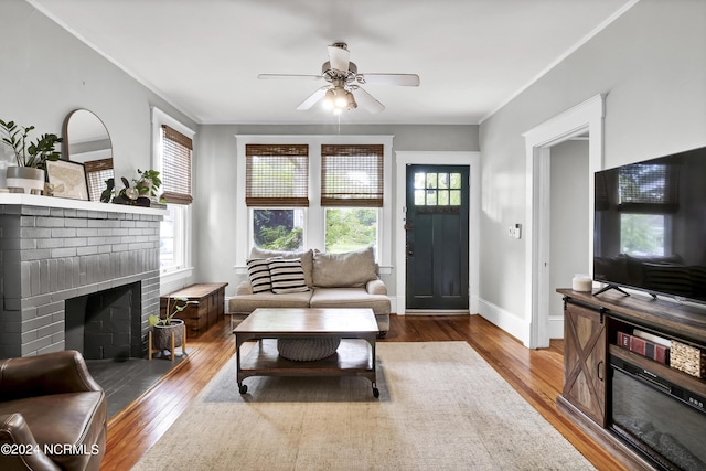 living room with hardwood / wood-style flooring, ceiling fan, crown molding, and a brick fireplace