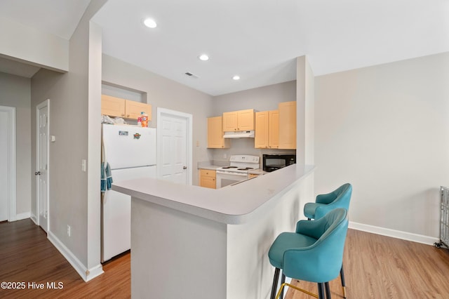 kitchen with light wood-type flooring, a kitchen bar, white appliances, and kitchen peninsula