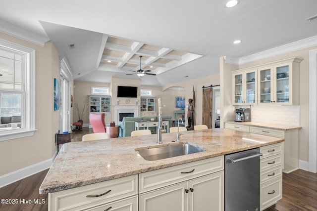 kitchen featuring coffered ceiling, ceiling fan, light stone counters, a barn door, and a center island with sink