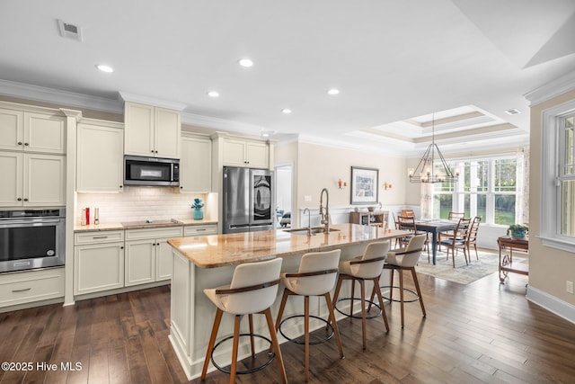 kitchen featuring sink, appliances with stainless steel finishes, backsplash, light stone counters, and a center island with sink