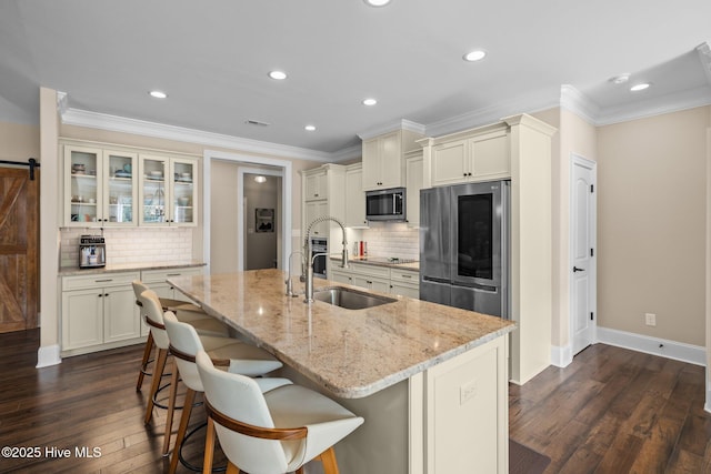 kitchen with light stone countertops, stainless steel appliances, a barn door, and a center island with sink