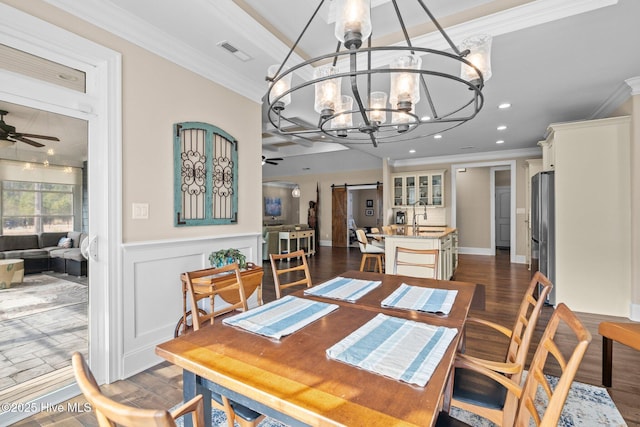 dining space featuring dark wood-type flooring, ornamental molding, a barn door, and ceiling fan with notable chandelier