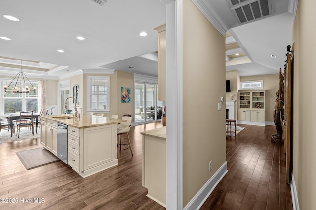 kitchen with dark wood-type flooring, a breakfast bar area, light stone counters, a tray ceiling, and a kitchen island with sink