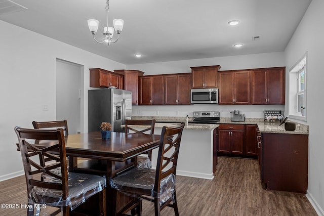 kitchen with decorative light fixtures, dark hardwood / wood-style flooring, a center island, light stone counters, and stainless steel appliances